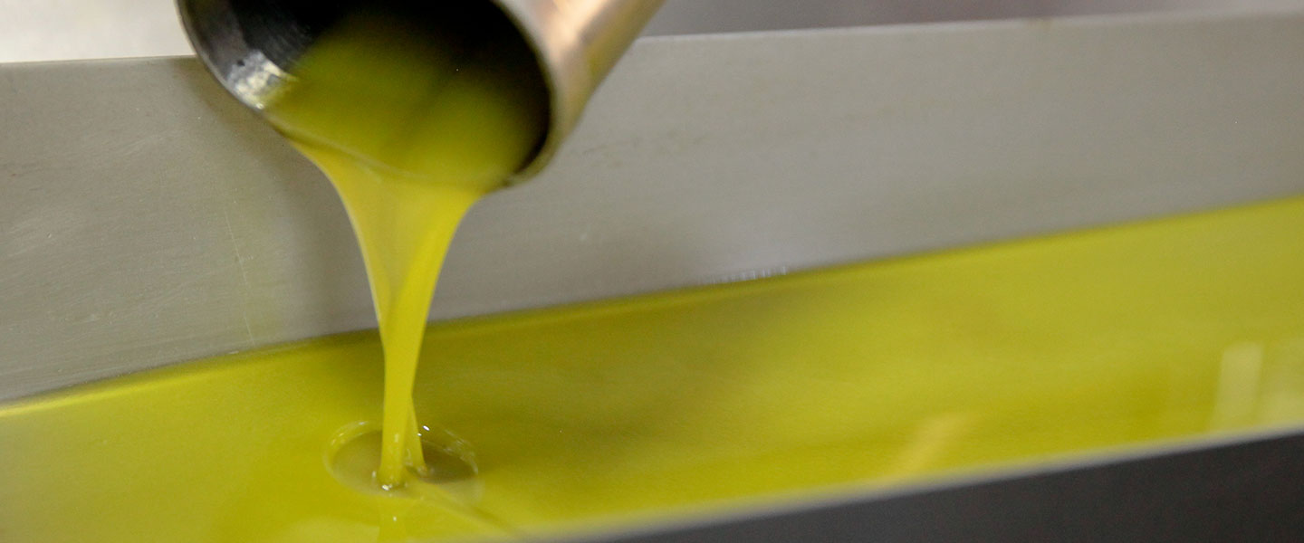 Freshly extracted green olive oil flowing from a stainless-steel spout.