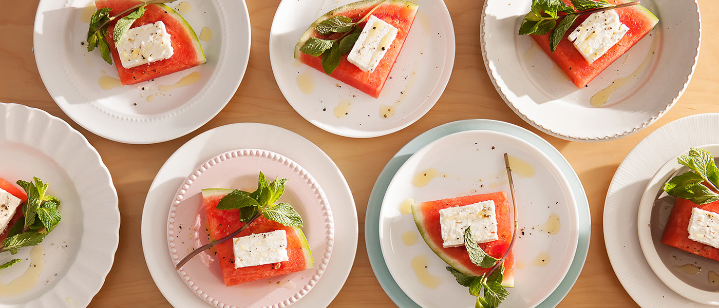 Plates of sliced watermelon topped with feta, fresh mint, black pepper, and drizzled olive oil.