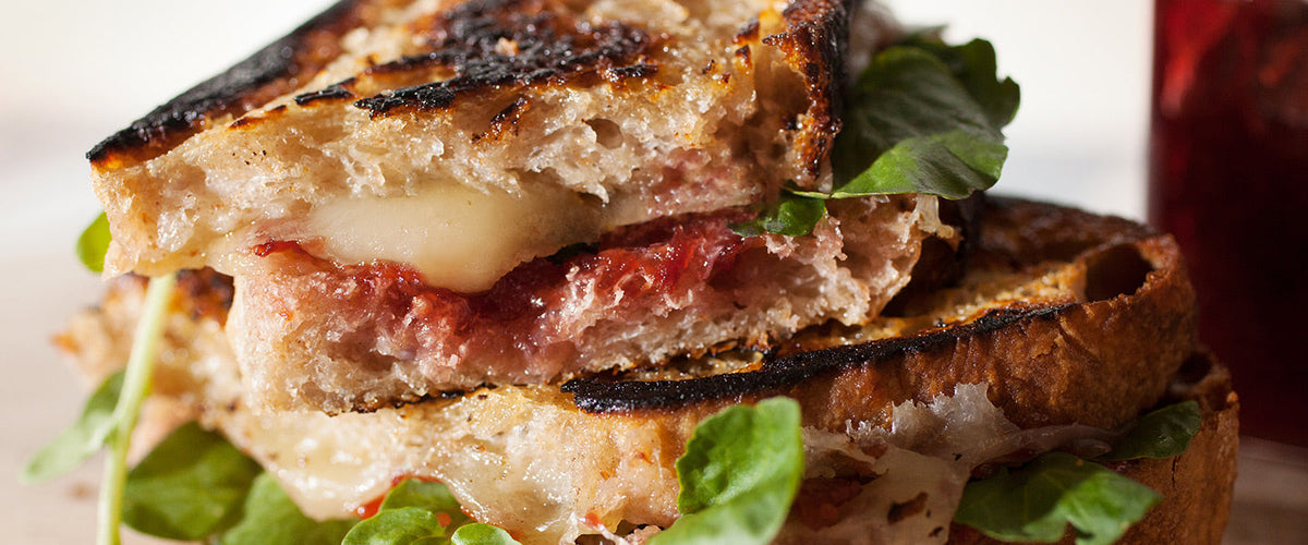 Grilled sandwich made with rustic bread, melted cheese, meat, fruit preserves, and fresh greens.