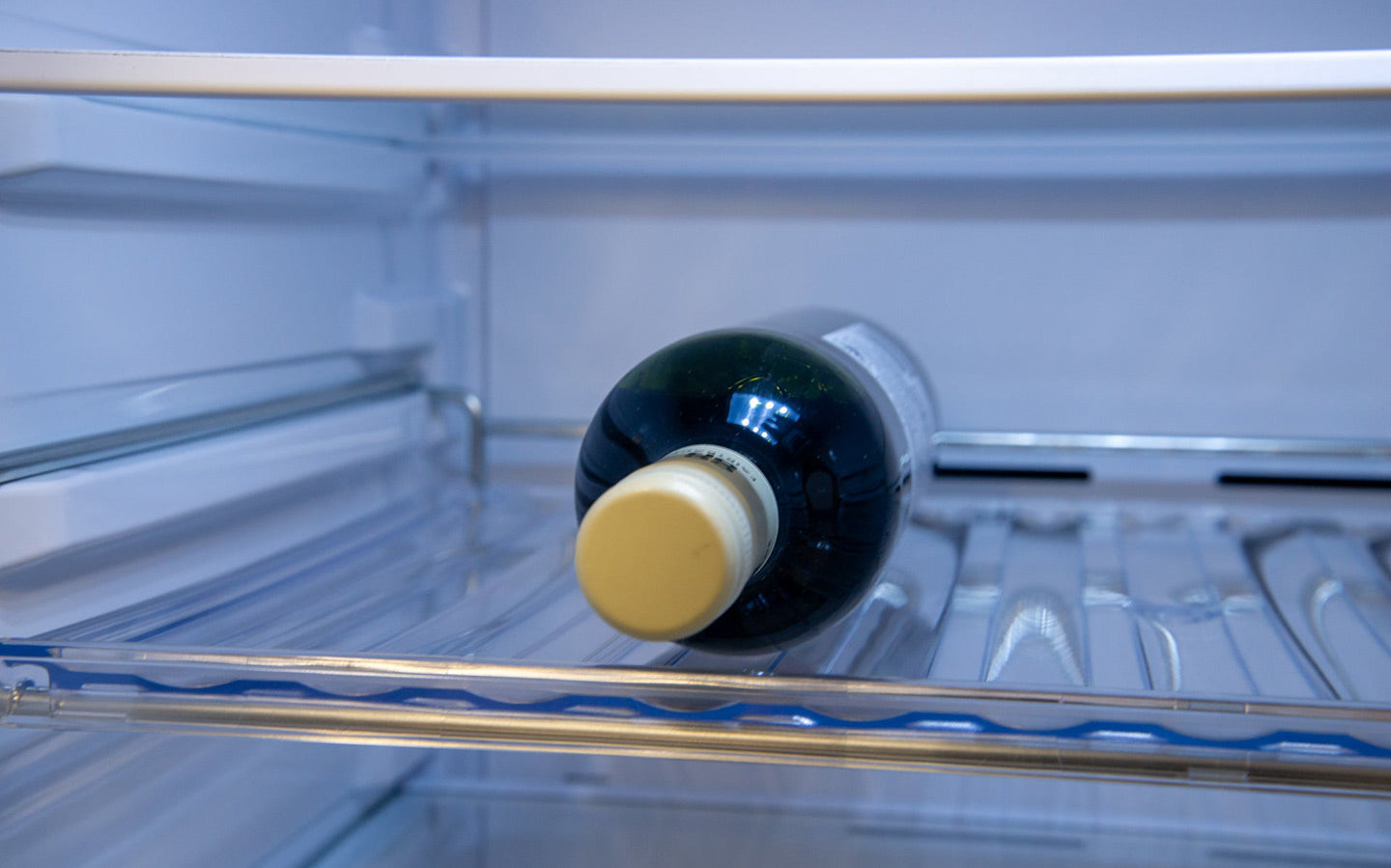 Glass bottle of olive oil stored on a shelf inside a refrigerator.