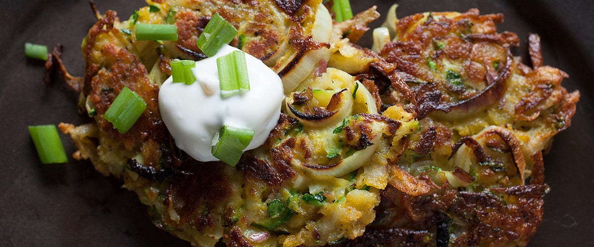 Crispy potato and zucchini latkes topped with sour cream and chopped green onions.