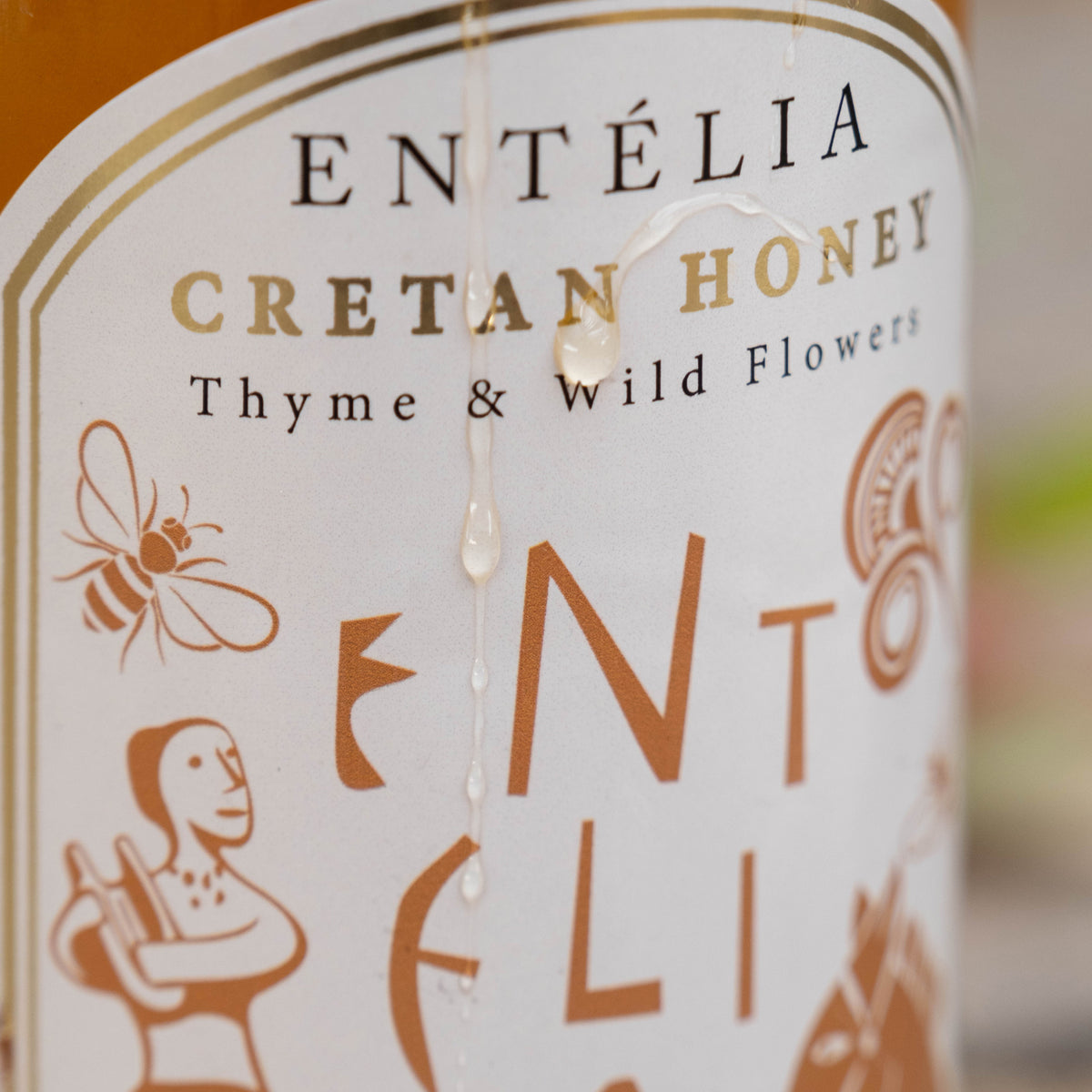 Honey droplets running over the label of an Entelia Thyme & Wild Flowers Cretan Honey jar.