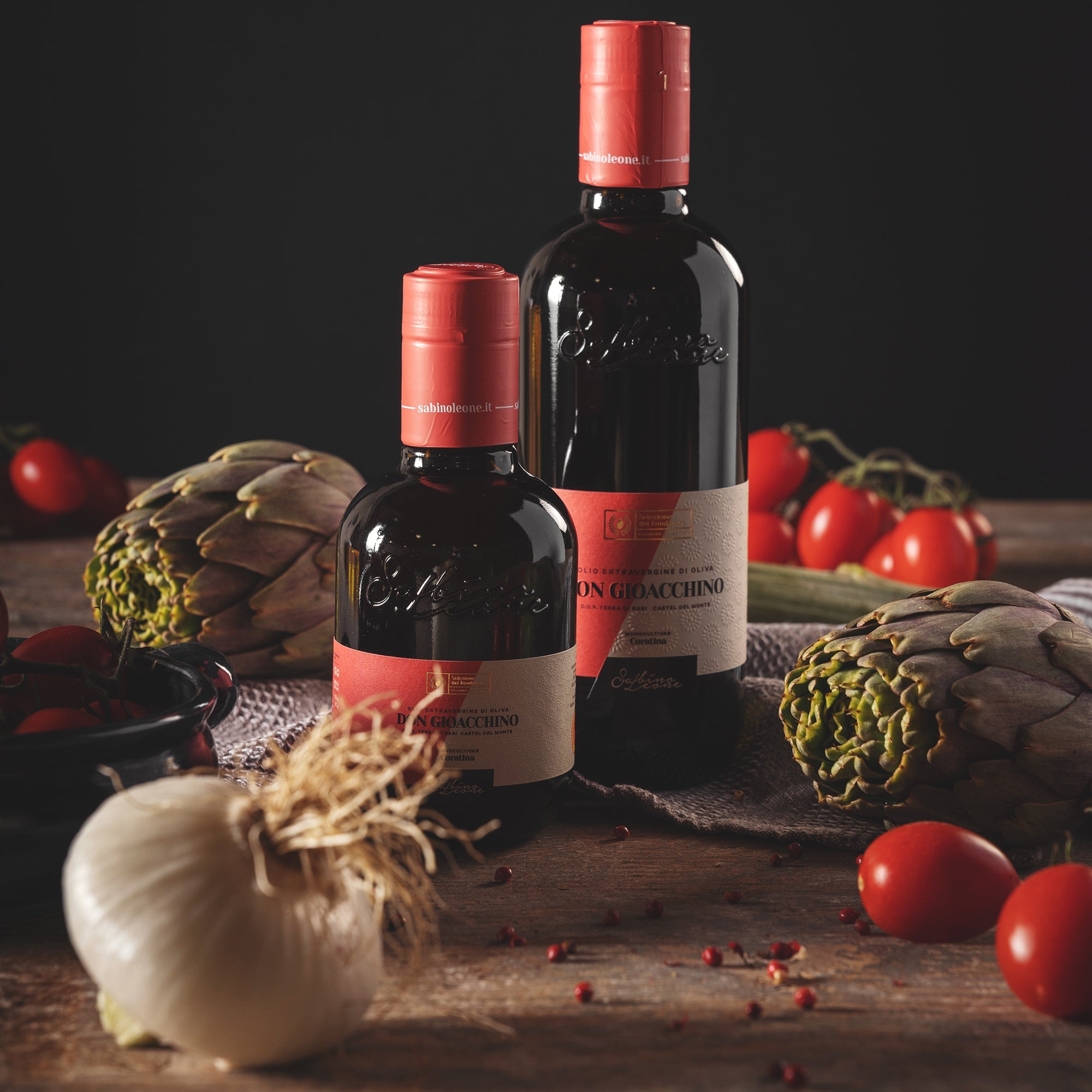 Sabino Leone Don Gioacchino olive oil bottles beside fresh artichokes, tomatoes, eggplant and garlic.