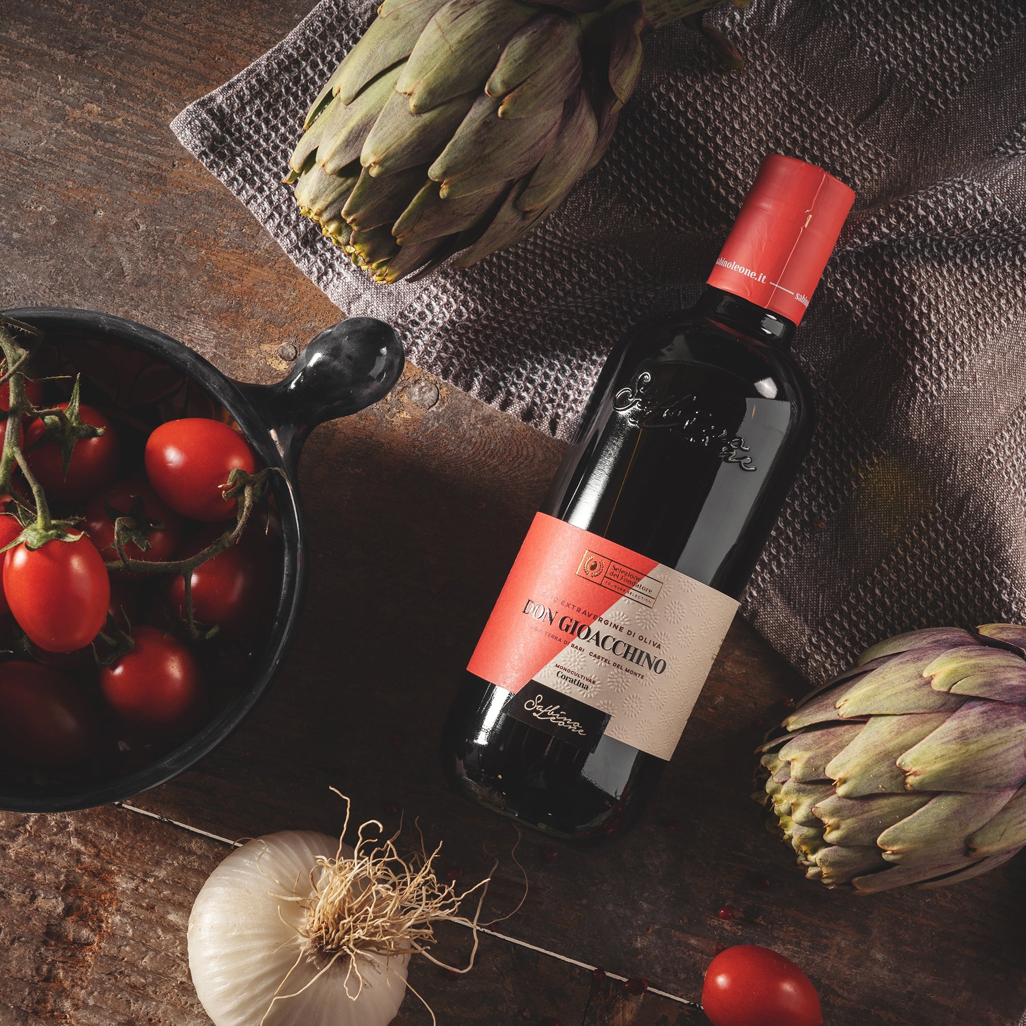 A Sabino Leone Don Gioacchino 500 ml bottle with artichokes, tomatoes and garlic on a table.