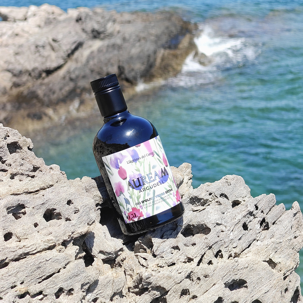Bottle of Auream Argudell on a rocky surface with water in the background