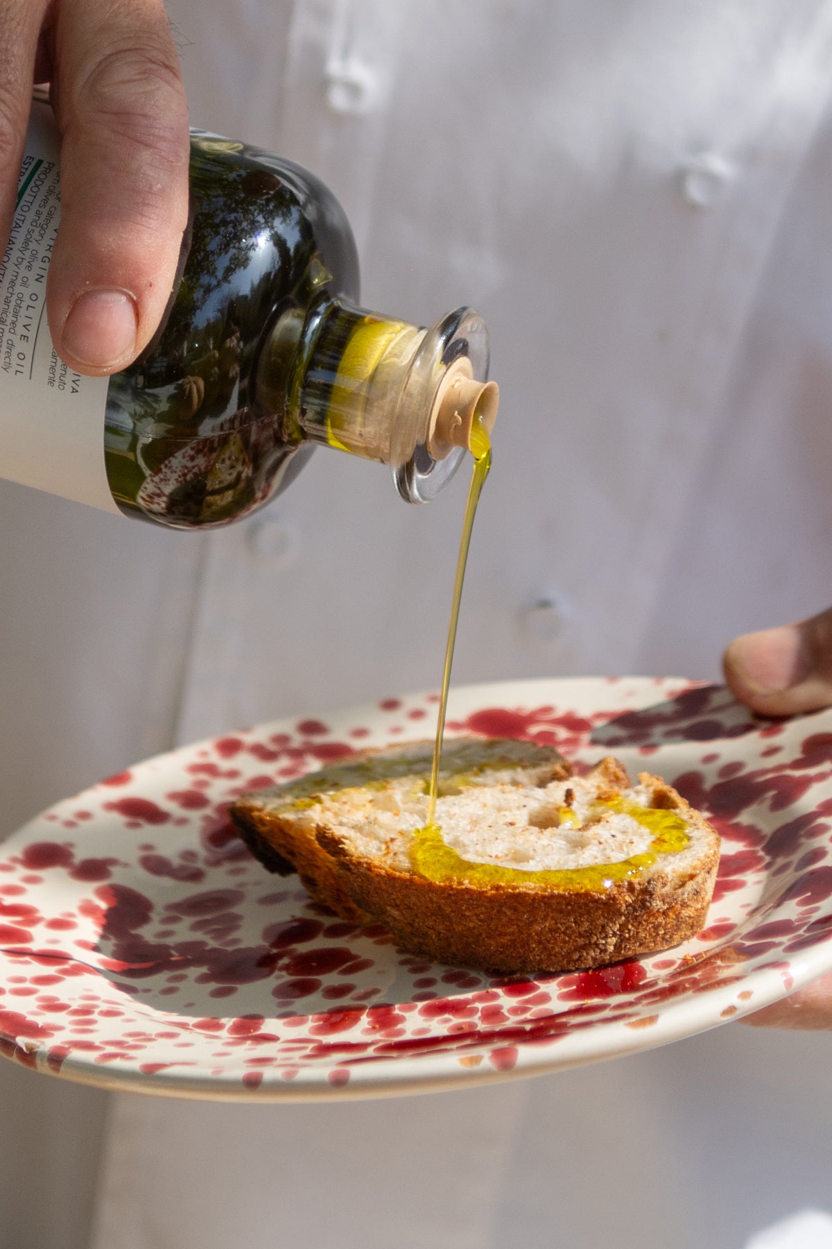 Person pouring olive oil onto bread on a patterned plate