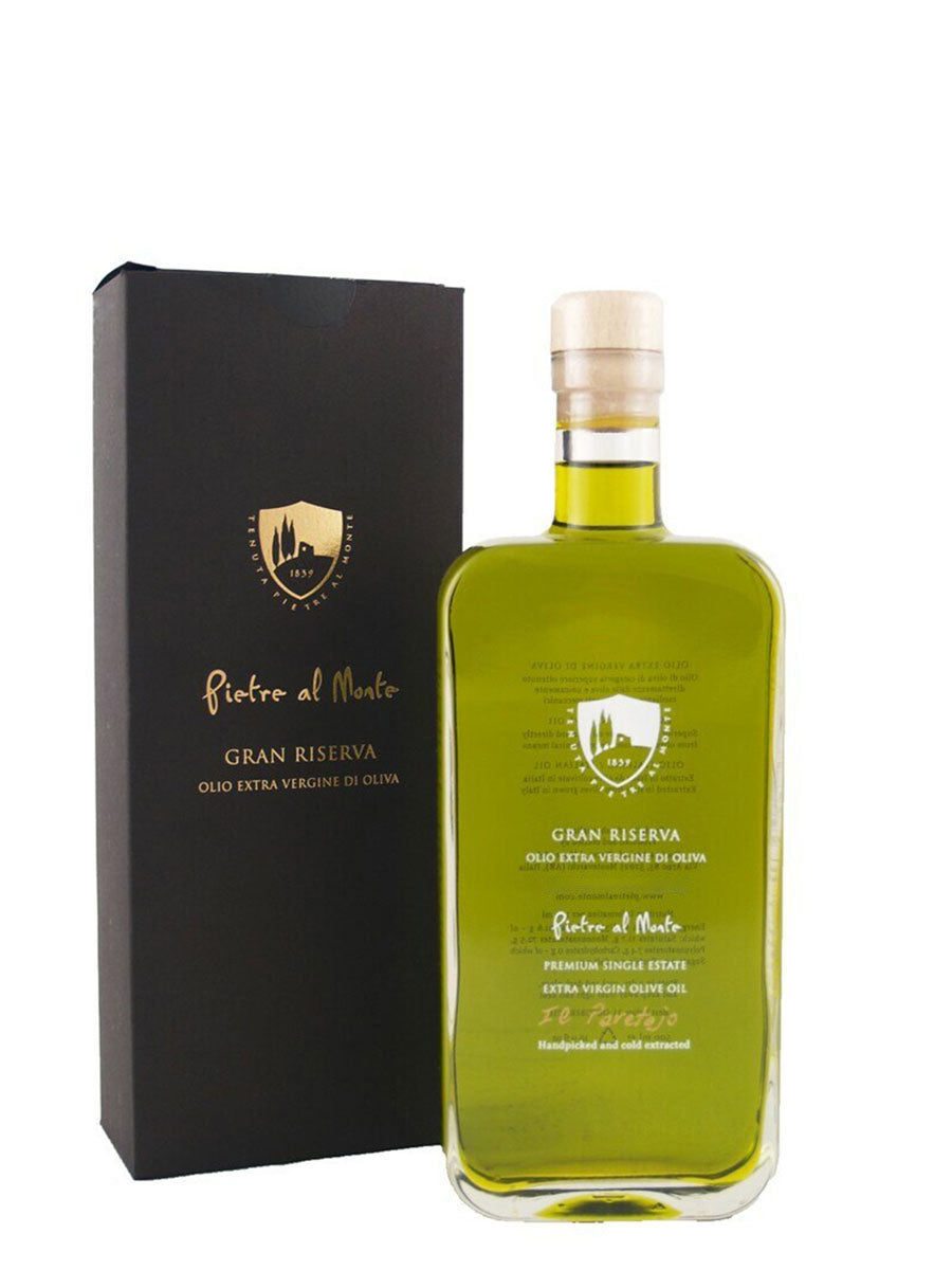 A bottle of Pietre al Monte Gran Riserva extra virgin olive oil with a black label and a clear bottle showing the green oil inside, accompanied by a black gift box with a gold emblem.