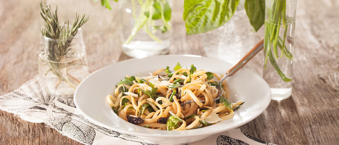Fresh herb linguine with sun-dried tomatoes and shaved cheese served in a white bowl.