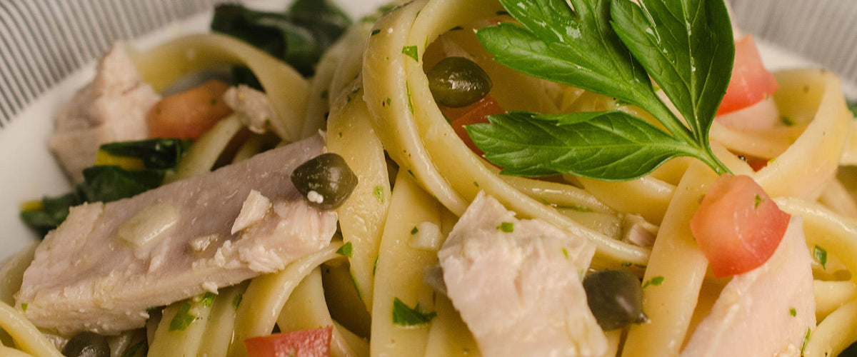 Pasta tonnato with thick noodles, tuna, capers, diced tomatoes, chopped herbs, and fresh basil.