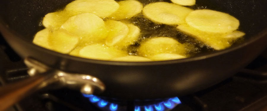 Thinly sliced potatoes frying in hot olive oil.