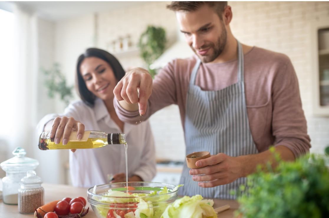man and woman pouring olive oil on homemade salad
